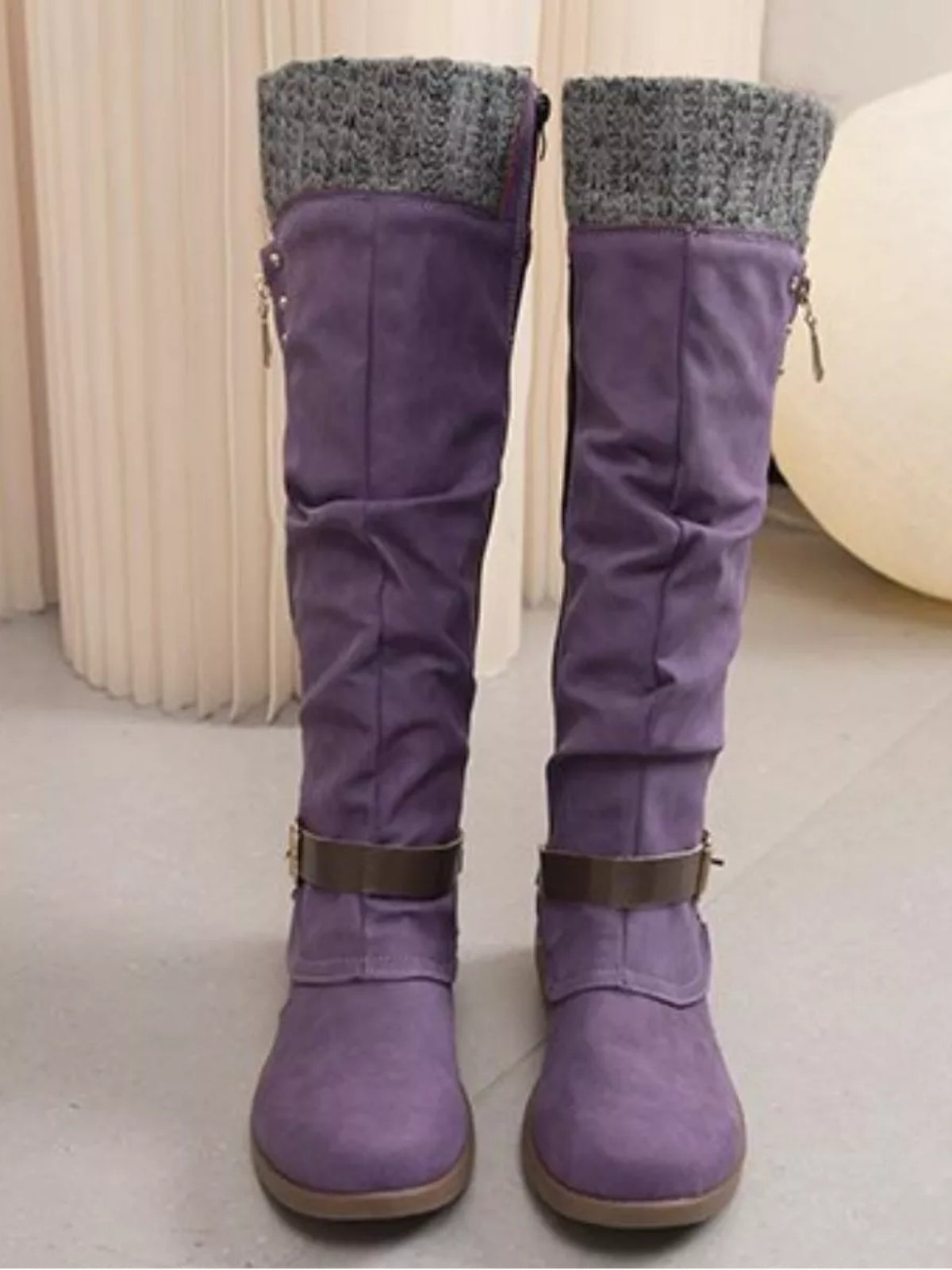 Purple suede knee-high slouch boots feature chunky gray knit cuffs, low heels, rounded toes, dark ankle straps, and rubber soles.