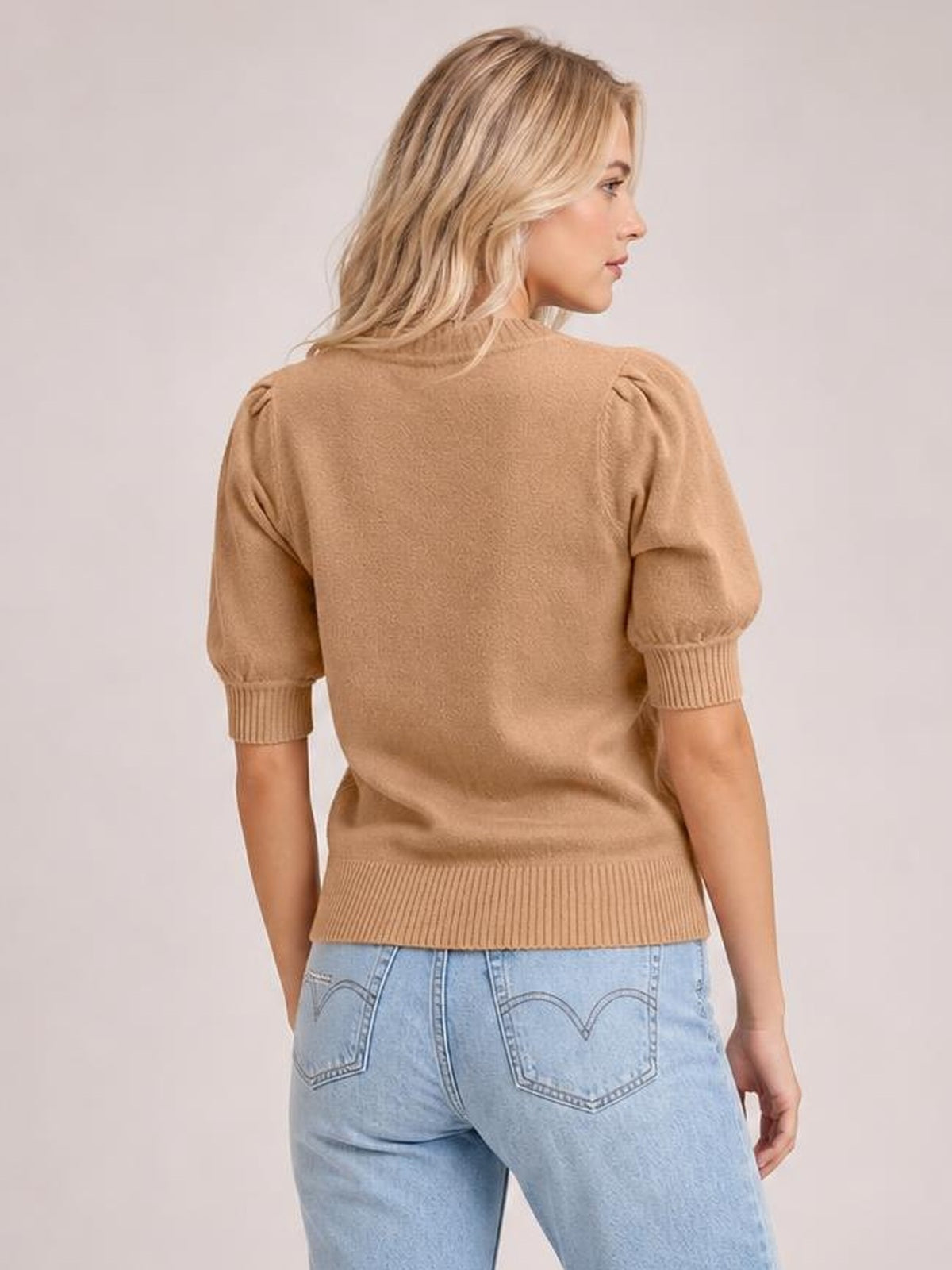 Model shown from the back in a camel knit sweater with short puff sleeves, ribbed cuffs and hem, and a relaxed silhouette.