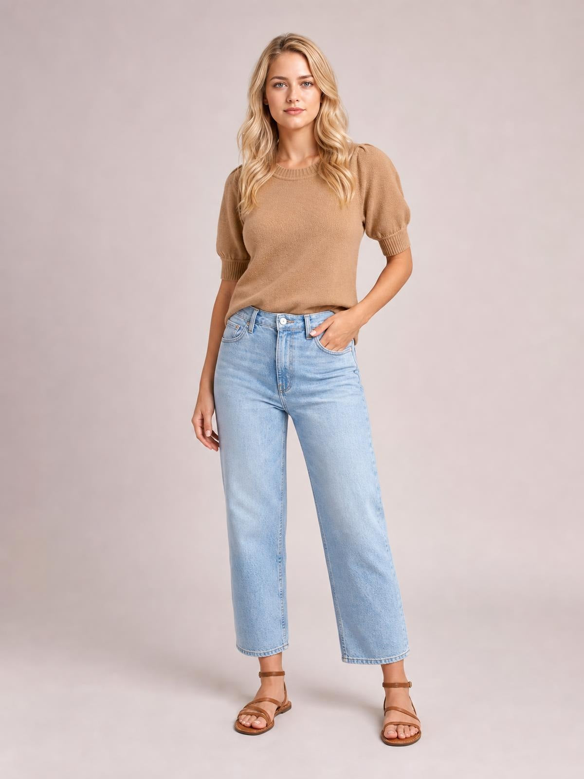 Model wearing a camel knit short puff sleeve sweater with a ribbed crew neckline, cuffs, and relaxed straight silhouette, posing with one hand in her jeans pocket.