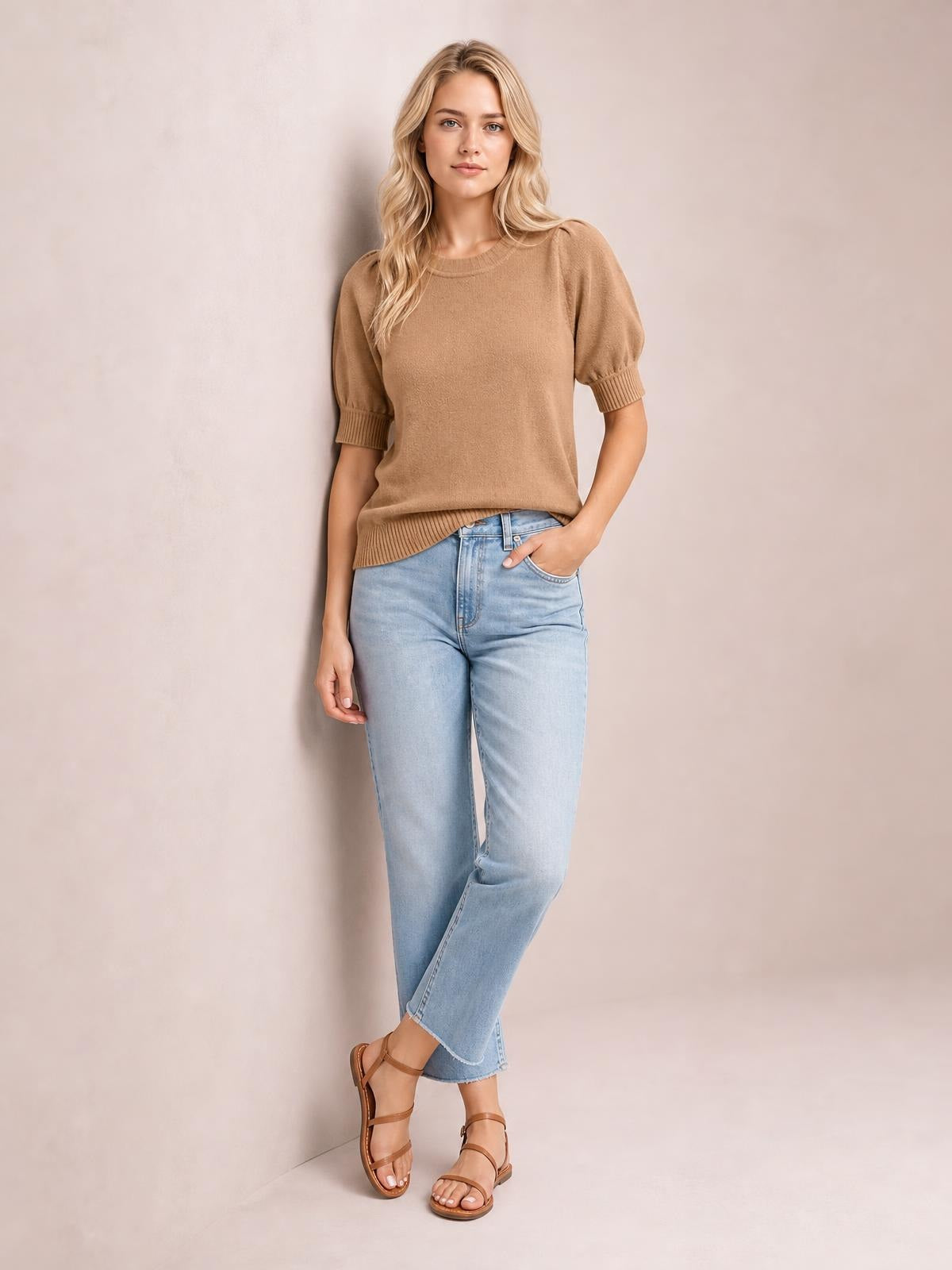 Model poses in a camel knit sweater with short puff sleeves, ribbed cuffs and hem, a crew neckline, and a relaxed straight silhouette.