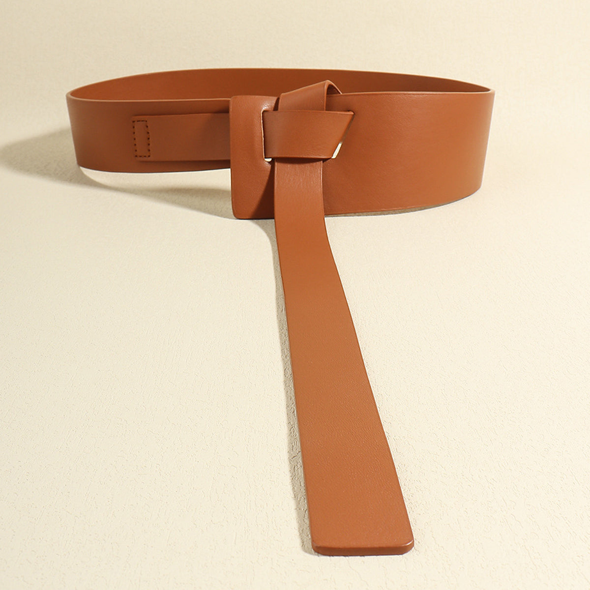 Brown PU knot detail belt with a broad wraparound silhouette, sculptural front construction, and an extended strap that drapes vertically.