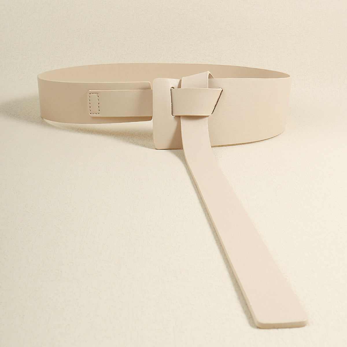 Wide beige PU belt with a broad wraparound silhouette, sculptural knot detail at the front, and an extended strap draping vertically.