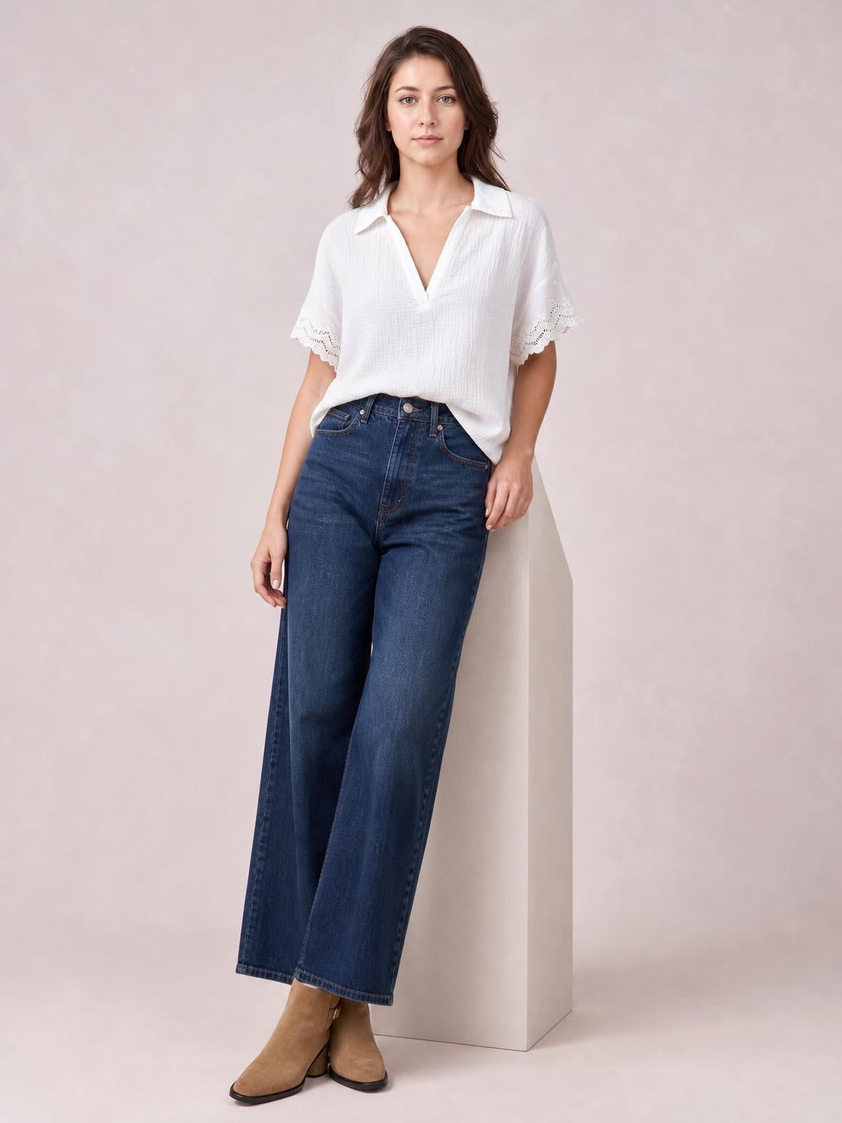 Model poses in a white collared short-sleeve blouse with lace-trimmed cuffs and a relaxed silhouette, paired with wide-leg dark blue jeans.