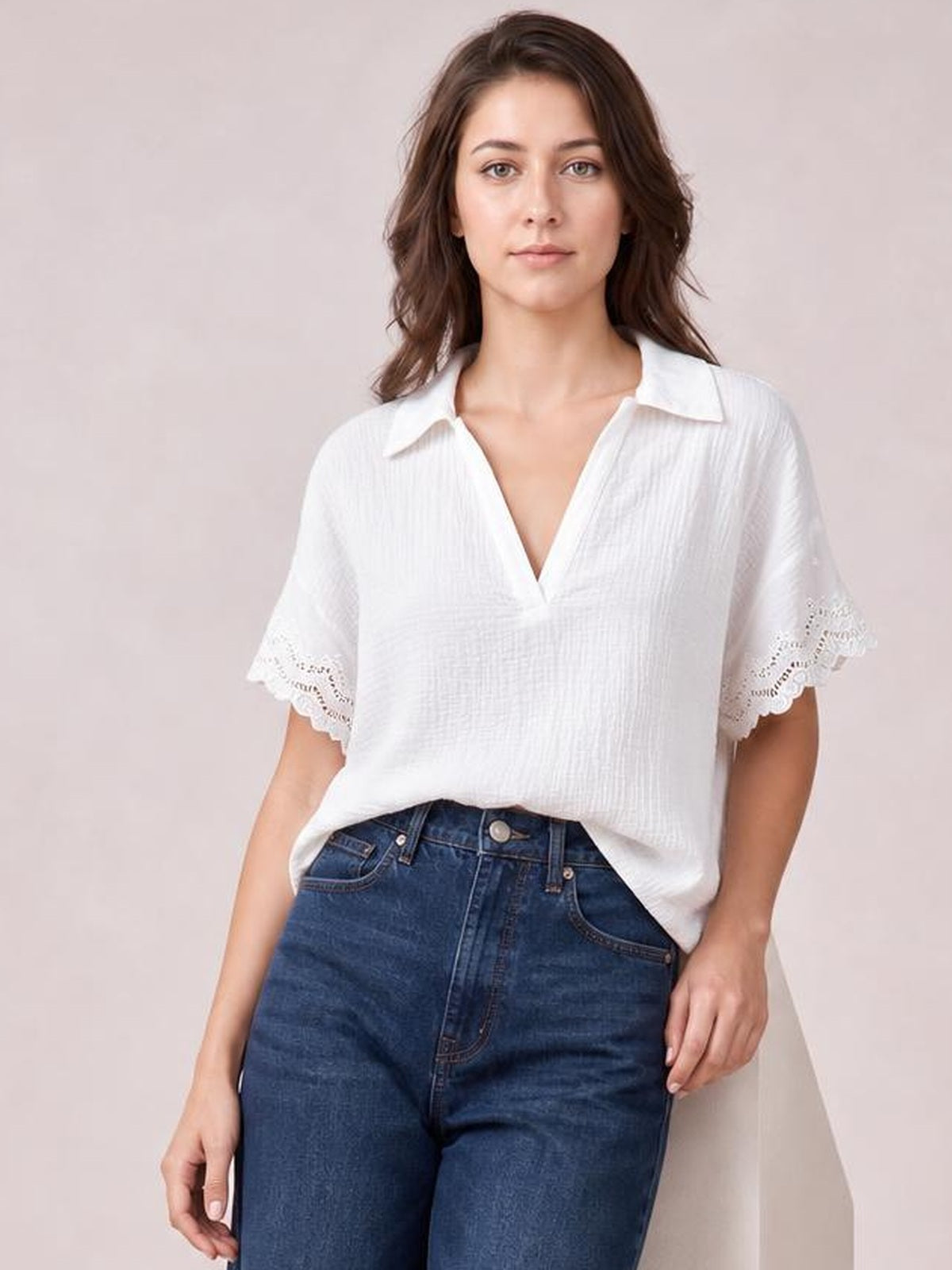Model wearing a white collared short-sleeve blouse with lace-trimmed cuffs, a relaxed straight silhouette, and a V-neck opening, paired with jeans.