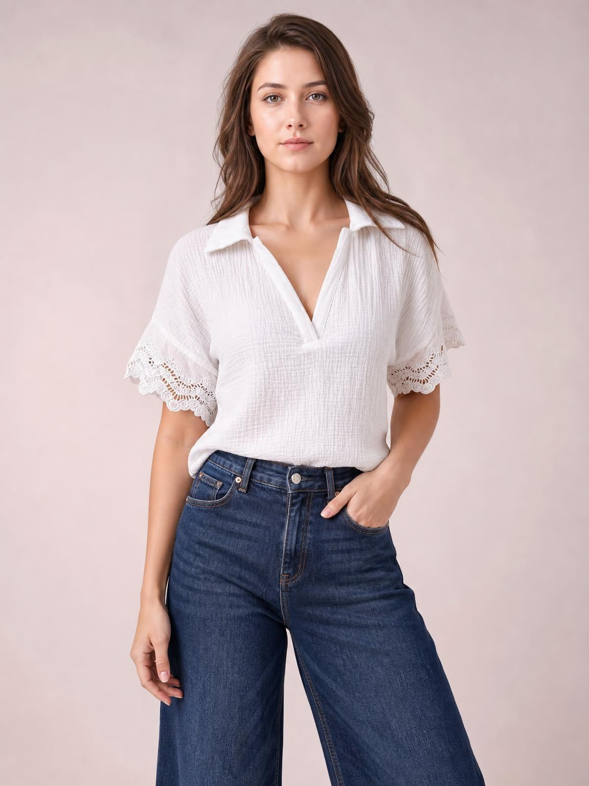 A model poses front-facing in a white collared short-sleeve blouse with a relaxed silhouette, V-neck opening, textured fabric, and elegant lace-trimmed cuffs.