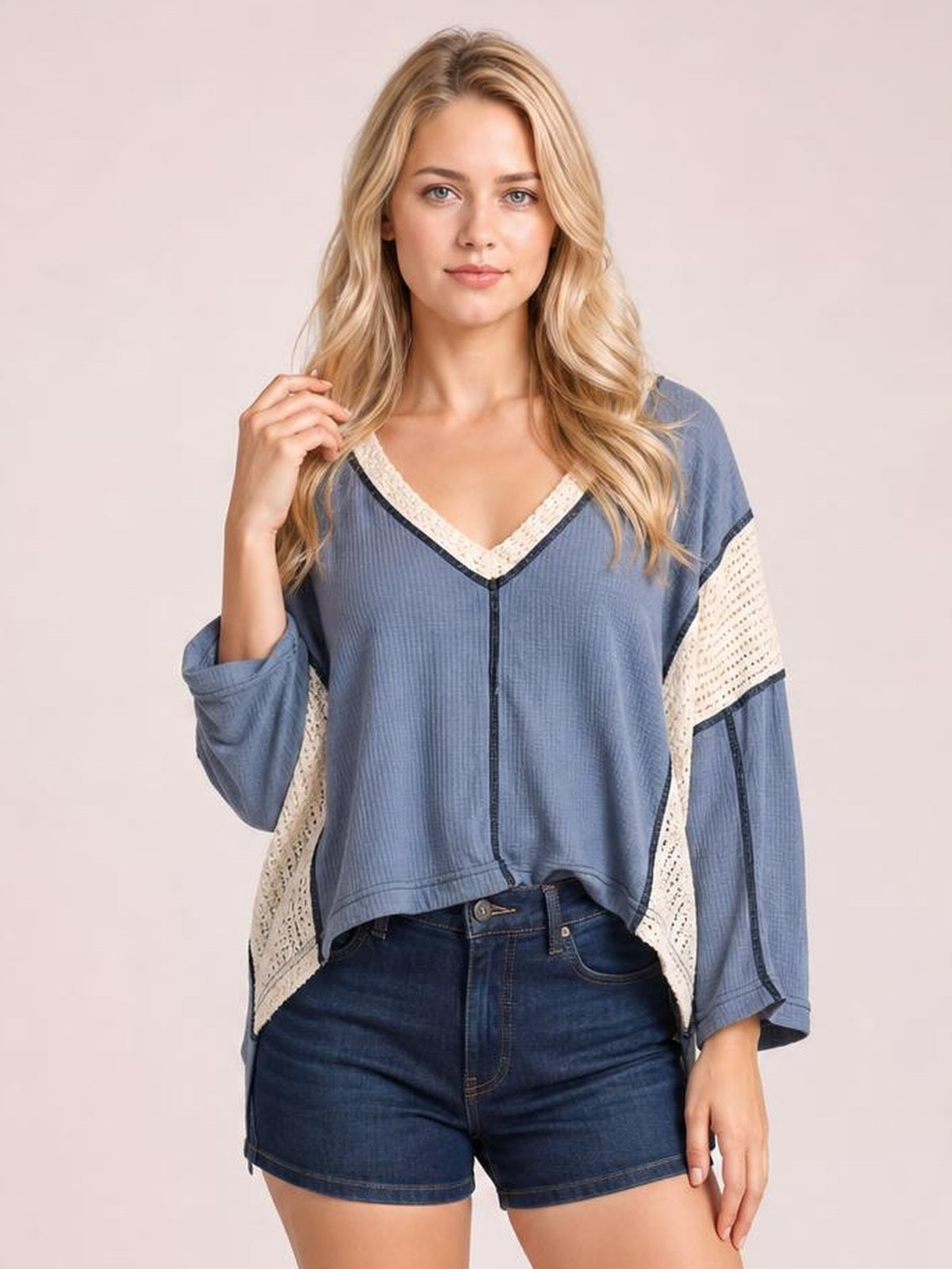 A woman poses in a blue long-sleeve blouse with a contrast cream lace V-neck, lace sleeve panels, relaxed fit, and straight hem.