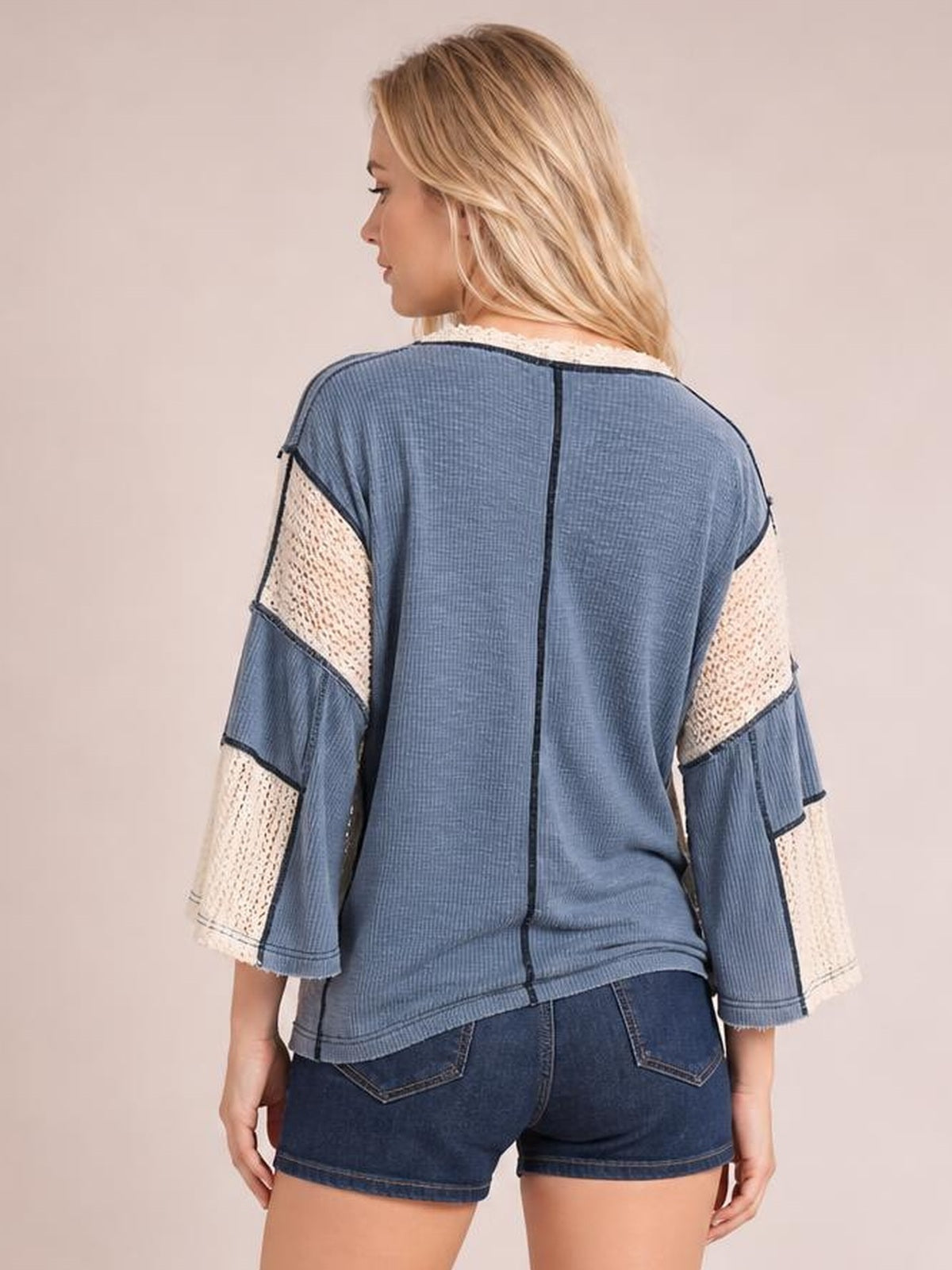 Back view of a model wearing a blue contrast blouse with lace-detail three-quarter sleeves, exposed seam construction, and a relaxed straight silhouette.