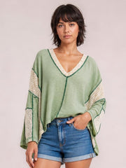 Model wears a sage green contrast V-neck blouse with cream lace trim and sleeve panels, long sleeves, and a relaxed oversized silhouette.