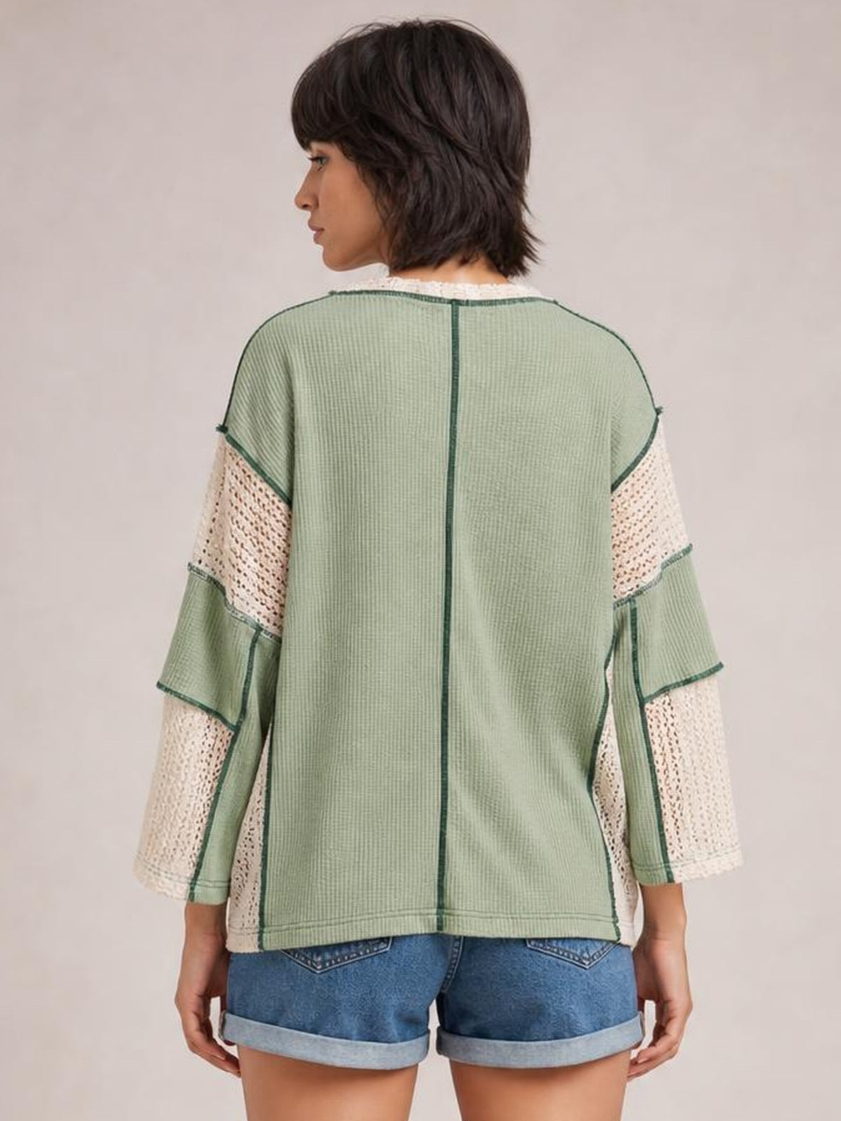 Model shown from the back wearing a sage green contrast blouse with long sleeves, lace panels, dark seam detailing, and a relaxed straight silhouette.