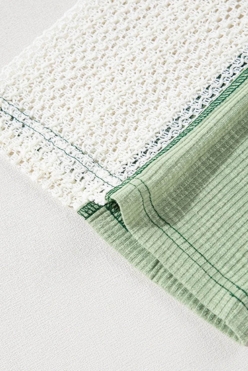 Close-up of the blouse’s cream textured lace detail contrasting with sage green ribbed fabric and dark green stitching along the finished seam.