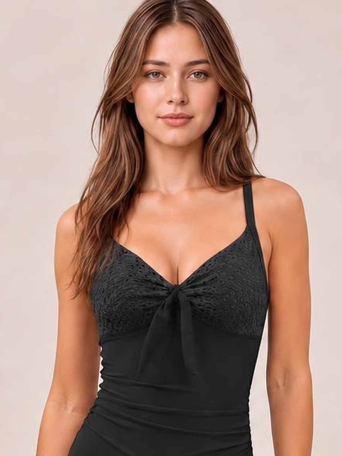 Model wearing a black lace-detail one-piece swimsuit with thin straps, a sweetheart neckline, center tie, and ruched waist in a fitted silhouette.