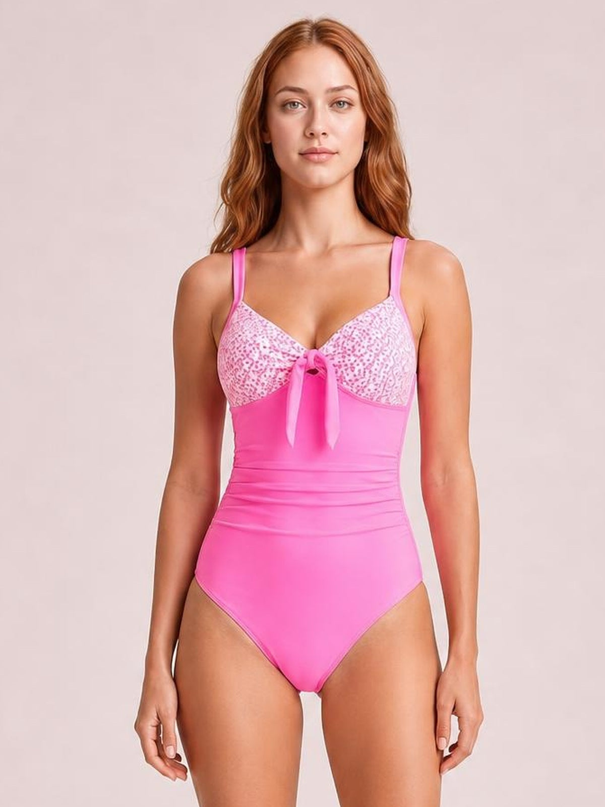 Standing model wears a bright pink one-piece swimsuit with lace-detail cups, shoulder straps, a center tie, ruched waist, and a high-cut silhouette.
