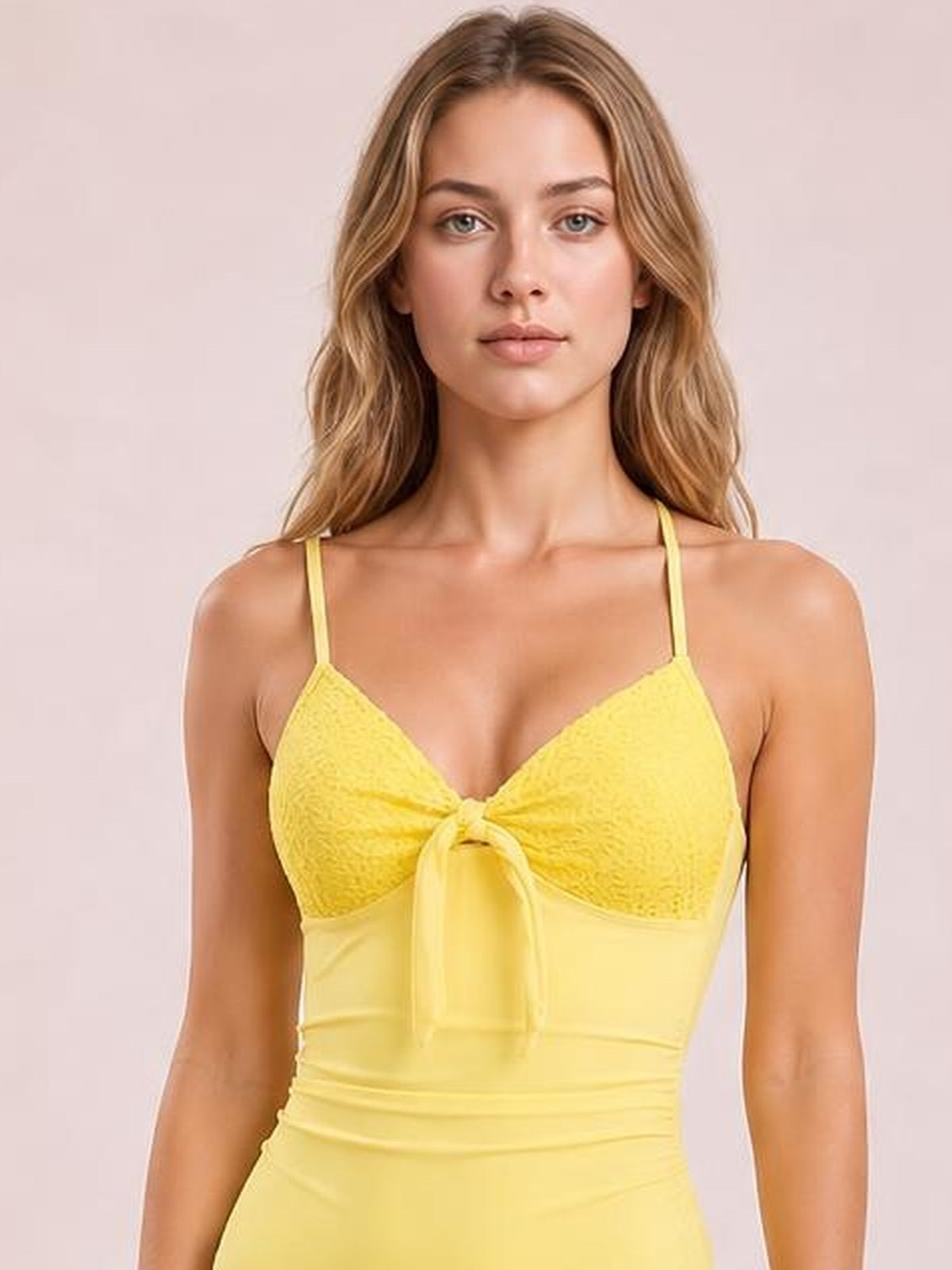 Model wears a yellow one-piece swimsuit with lace-detail cups, thin shoulder straps, a front tie, and a fitted, stretchy silhouette.