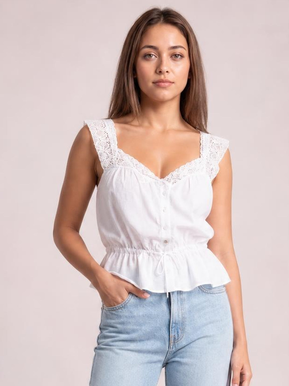 Model poses with one hand in her jeans pocket wearing a white lace-detail tank with button accents, adjustable drawstring waist, wide straps, and a peplum silhouette.