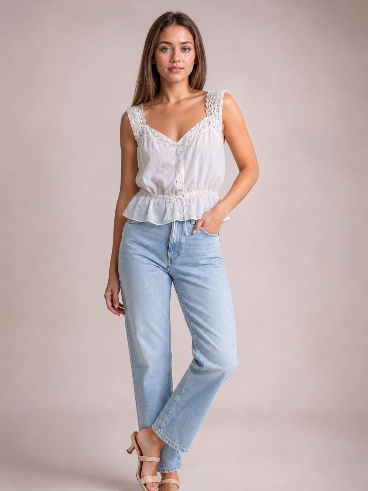 A model poses with one hand in her pocket wearing a white lace-detail tank with button front, V-neckline, drawstring waist, and flared hem.