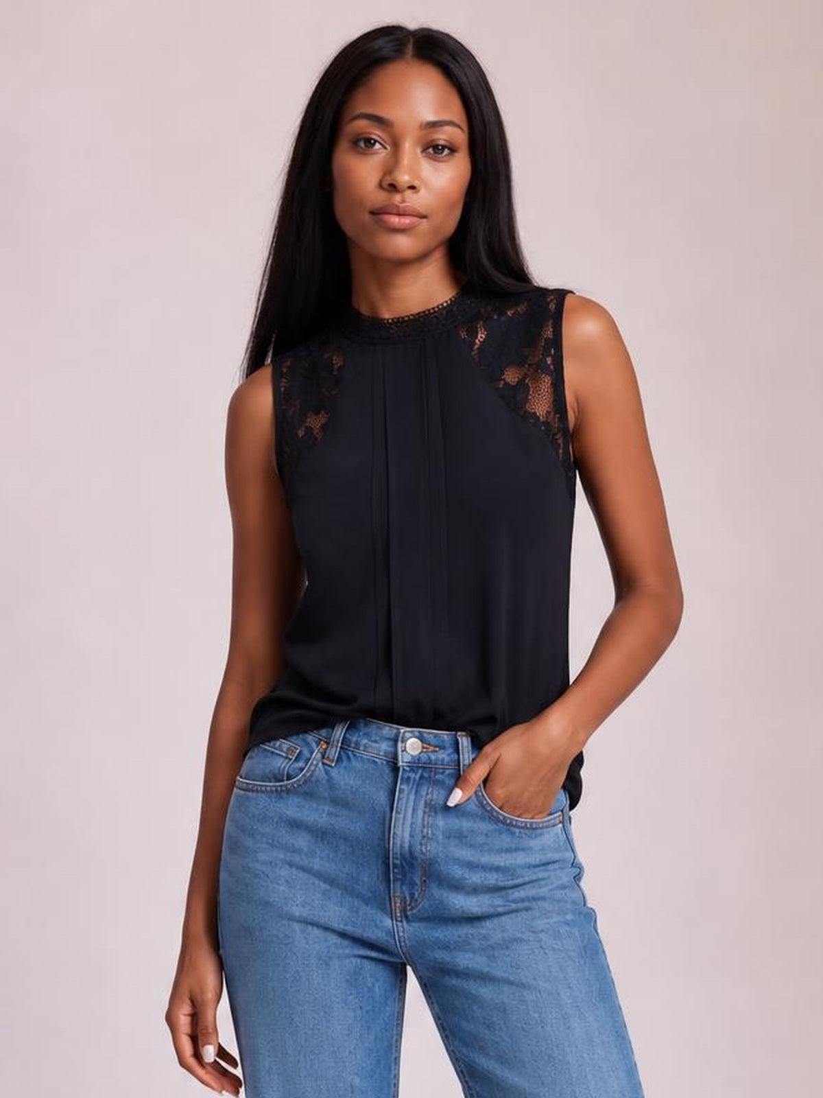 Model poses in a black semi-sheer lace detail mock neck sleeveless top with a relaxed silhouette and vertical front pleats.