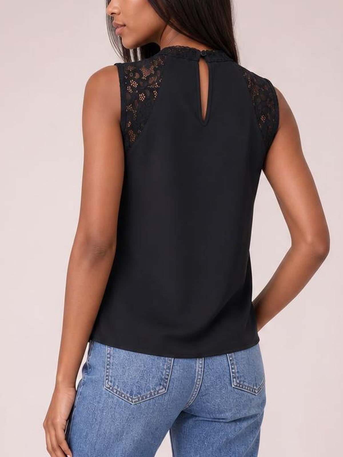 A model poses from behind in a black sleeveless mock neck top with semi-sheer lace shoulder panels, a keyhole back, and a relaxed straight silhouette.