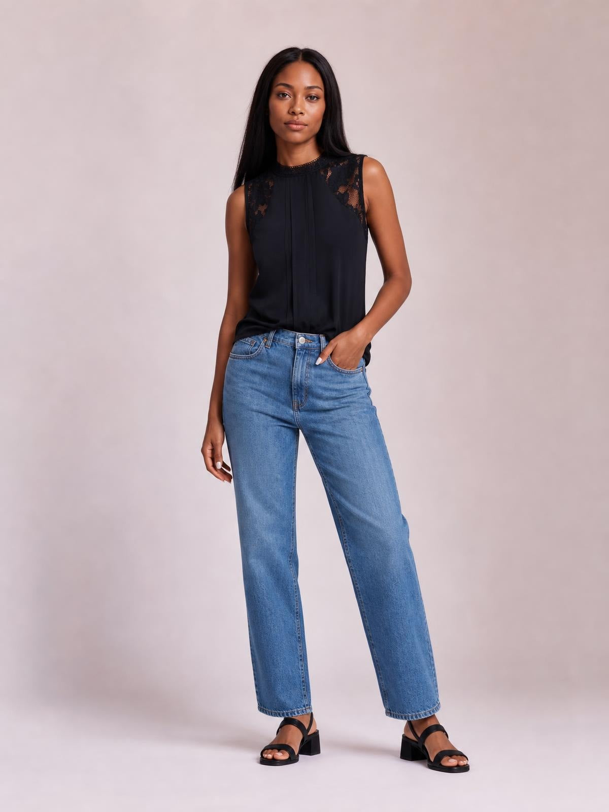 Model poses in a black semi-sheer sleeveless top with a mock neck, lace shoulder details, and a relaxed straight silhouette.