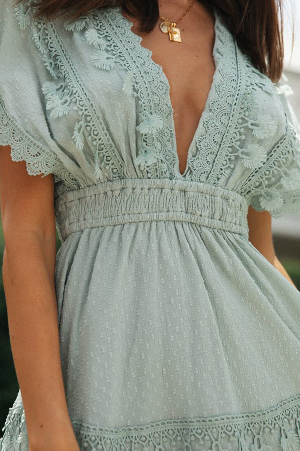 Model wearing a sage lace detail plunge mini dress with flutter short sleeves, a smocked waist, textured fabric, and delicate lace trim framing the bodice and skirt.