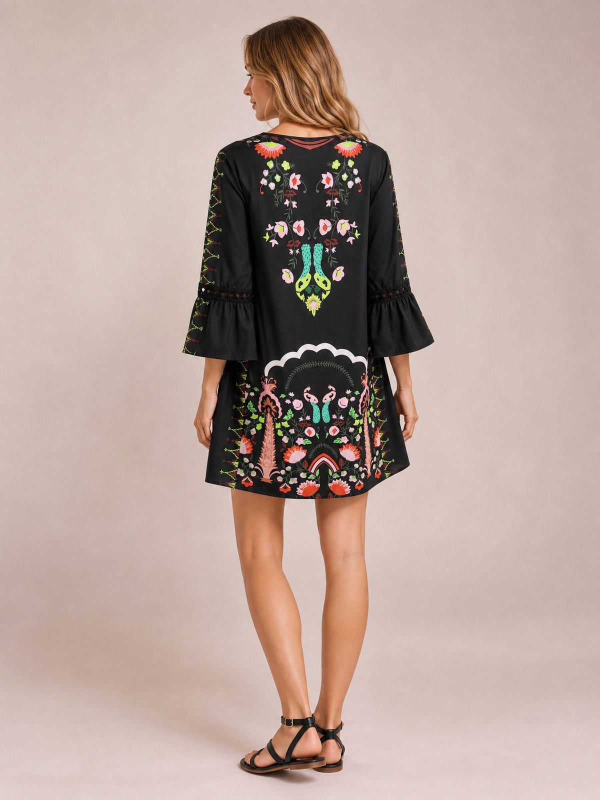 A model stands in a back view wearing a black printed dress with a softly flared short silhouette, three-quarter bell sleeves, and lace-trimmed sleeve bands.