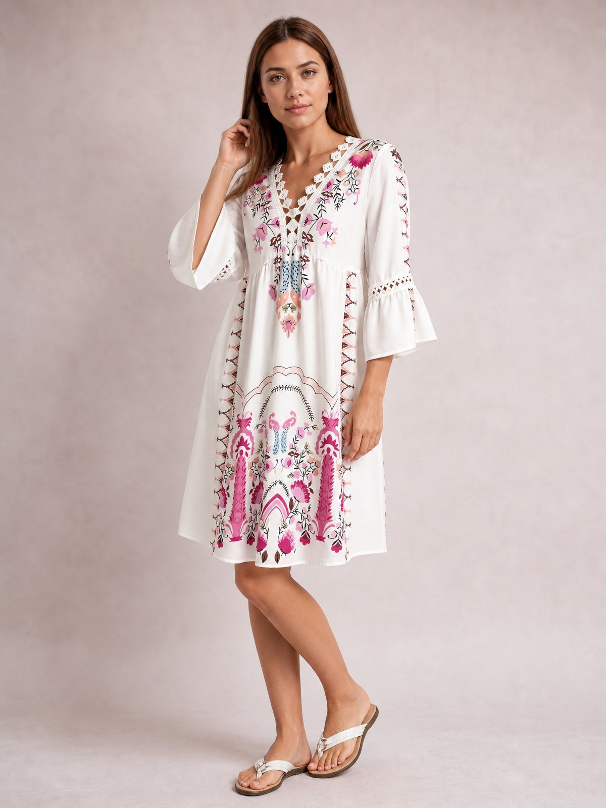 Model poses in a white printed dress with colorful floral motifs, lace-trimmed neckline and three-quarter bell sleeves, a gathered waist, and softly flared short silhouette.