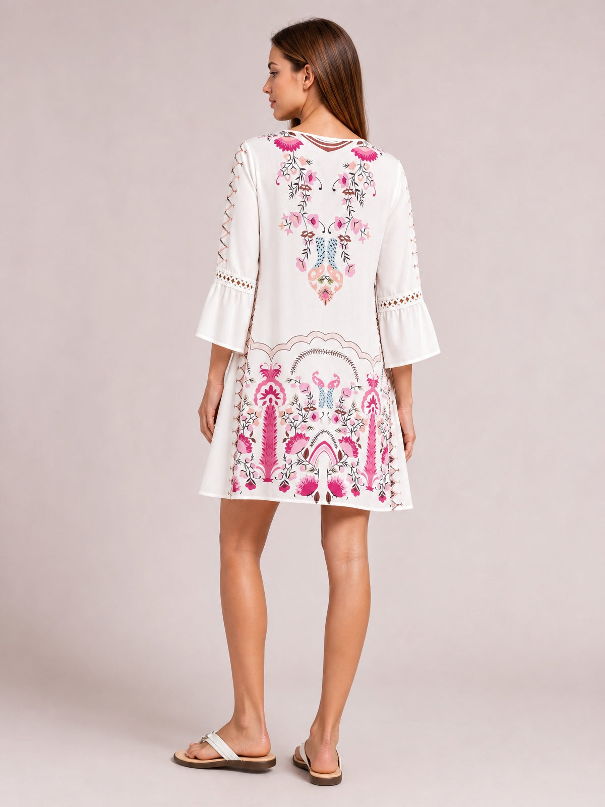 Model turned slightly away in a white printed dress with pink floral motifs, lace-trimmed three-quarter bell sleeves, a softly flared silhouette, and short hem.