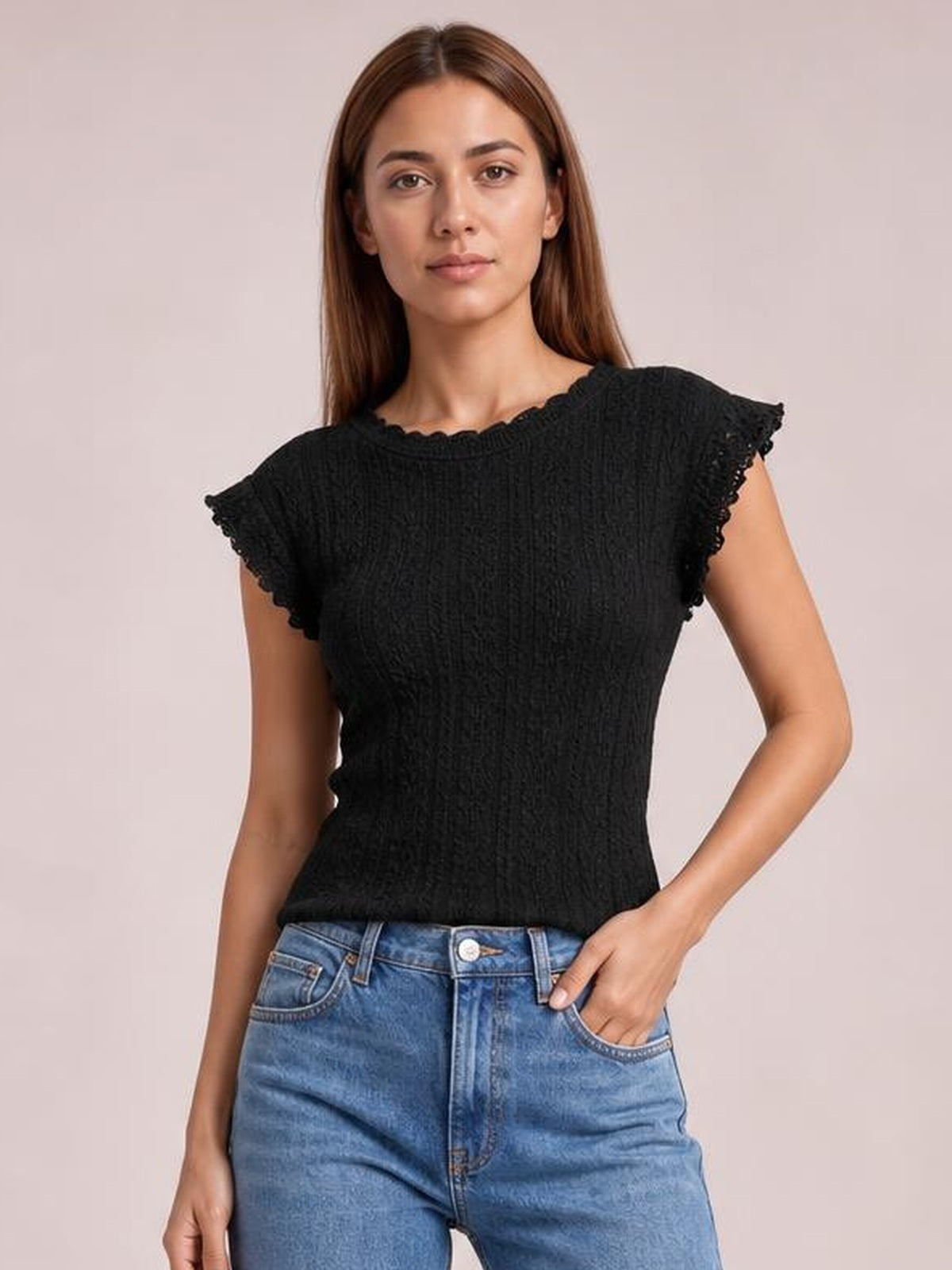 Model poses with one hand in her jeans pocket wearing a black lace detail round neck cap sleeve top with scalloped edges and a fitted silhouette.