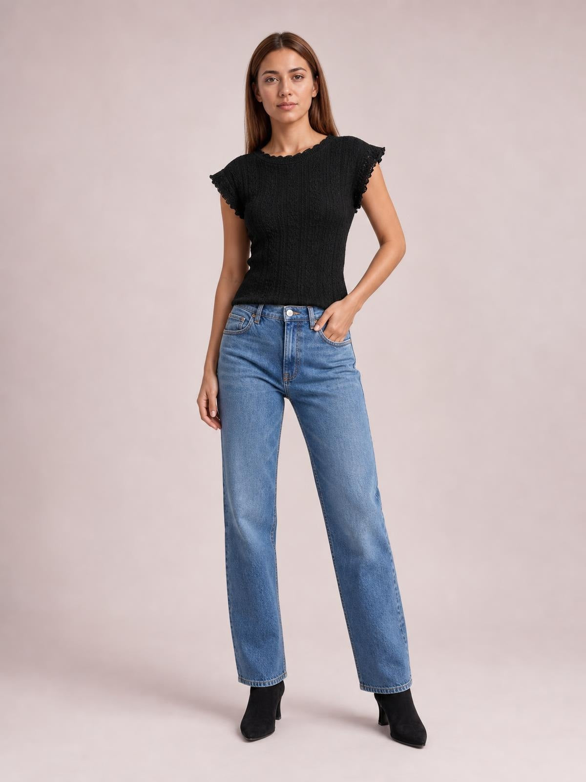 Model poses in a black lace detail round neck cap sleeve top with scalloped trim and a fitted silhouette, paired with jeans.