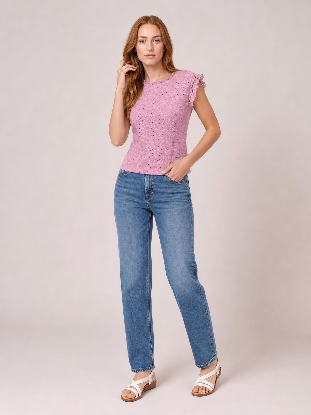 Model poses in a pink lace-detail round-neck cap-sleeve top with an eyelet texture, fitted silhouette, and scalloped sleeve edges.