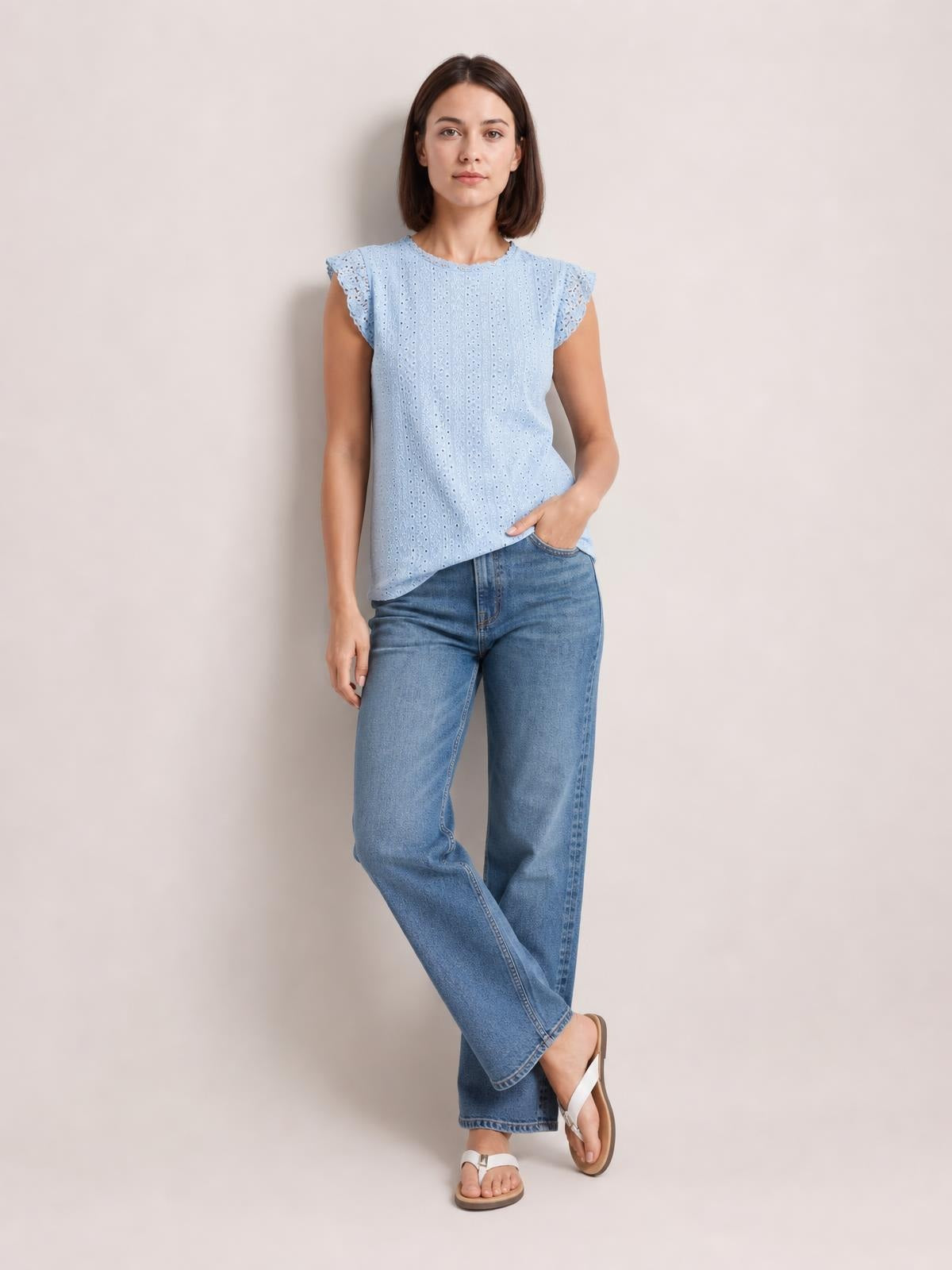 Model poses in a light blue eyelet lace detail top with a round neck, ruffled cap sleeves, relaxed silhouette, and straight hem.