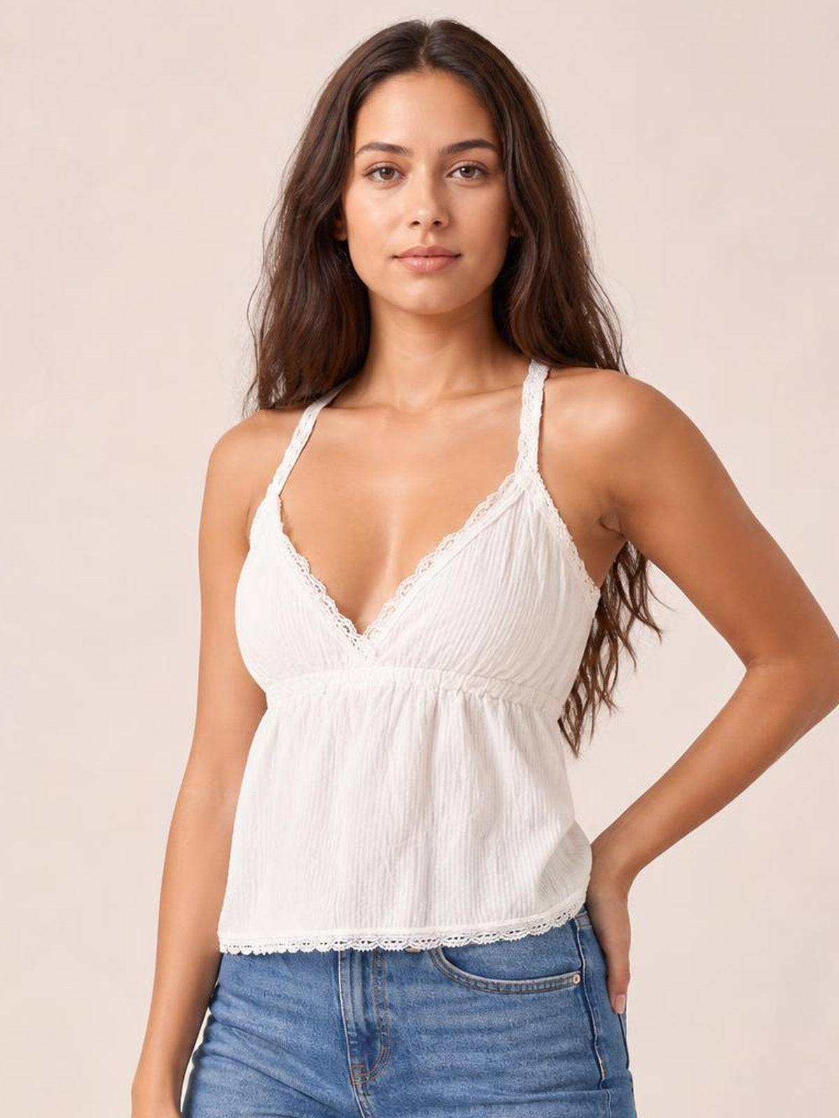 Model poses with one hand on her hip in a white lace detail V-neck cami featuring slim straps, a gathered waist, and relaxed silhouette.