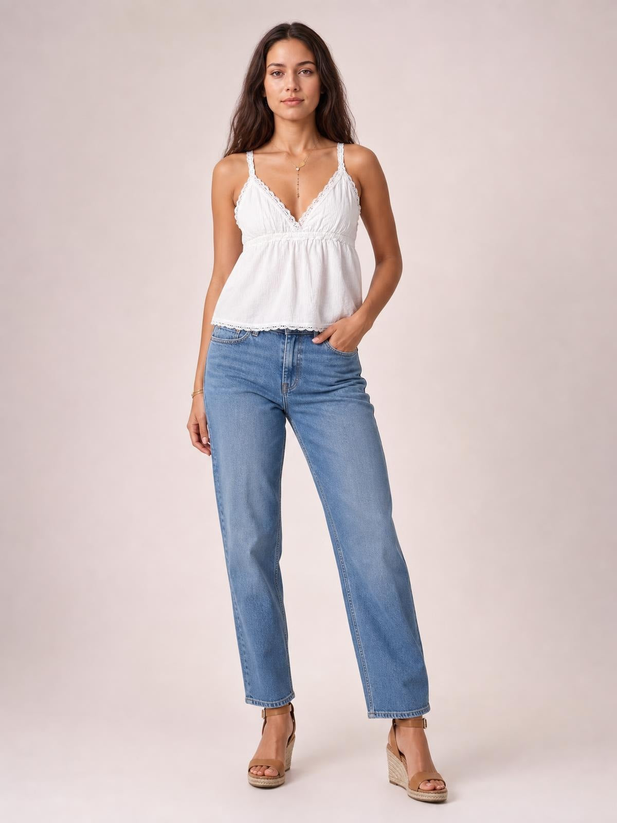 Model wears a white lace detail V-neck cami with thin straps, gathered bodice, relaxed silhouette, and scalloped hem, paired with jeans.