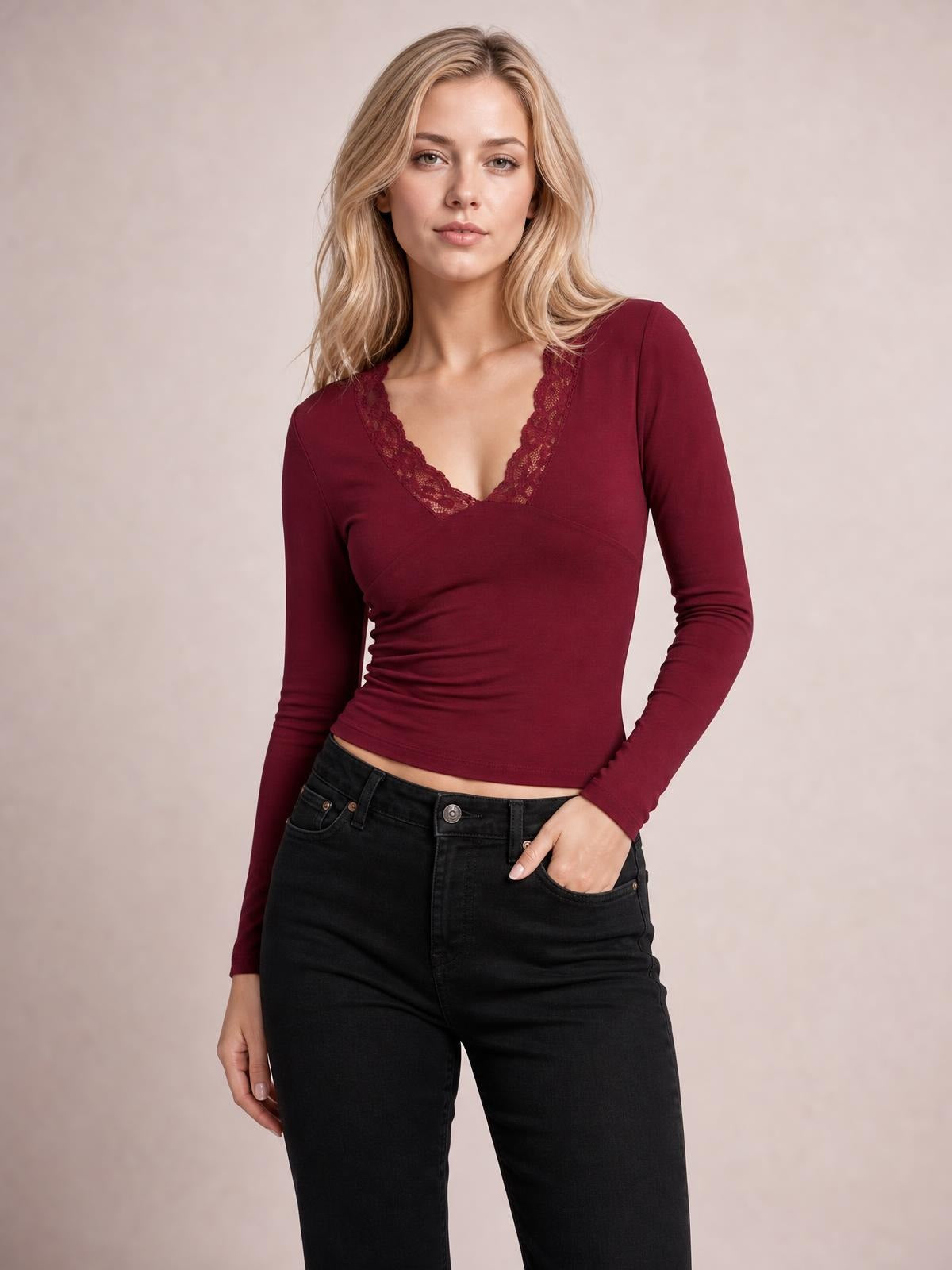 Model wears a burgundy lace detail V-neck long sleeve T-shirt with a fitted, slightly ruched silhouette and opaque stretch construction, one hand in her pocket.