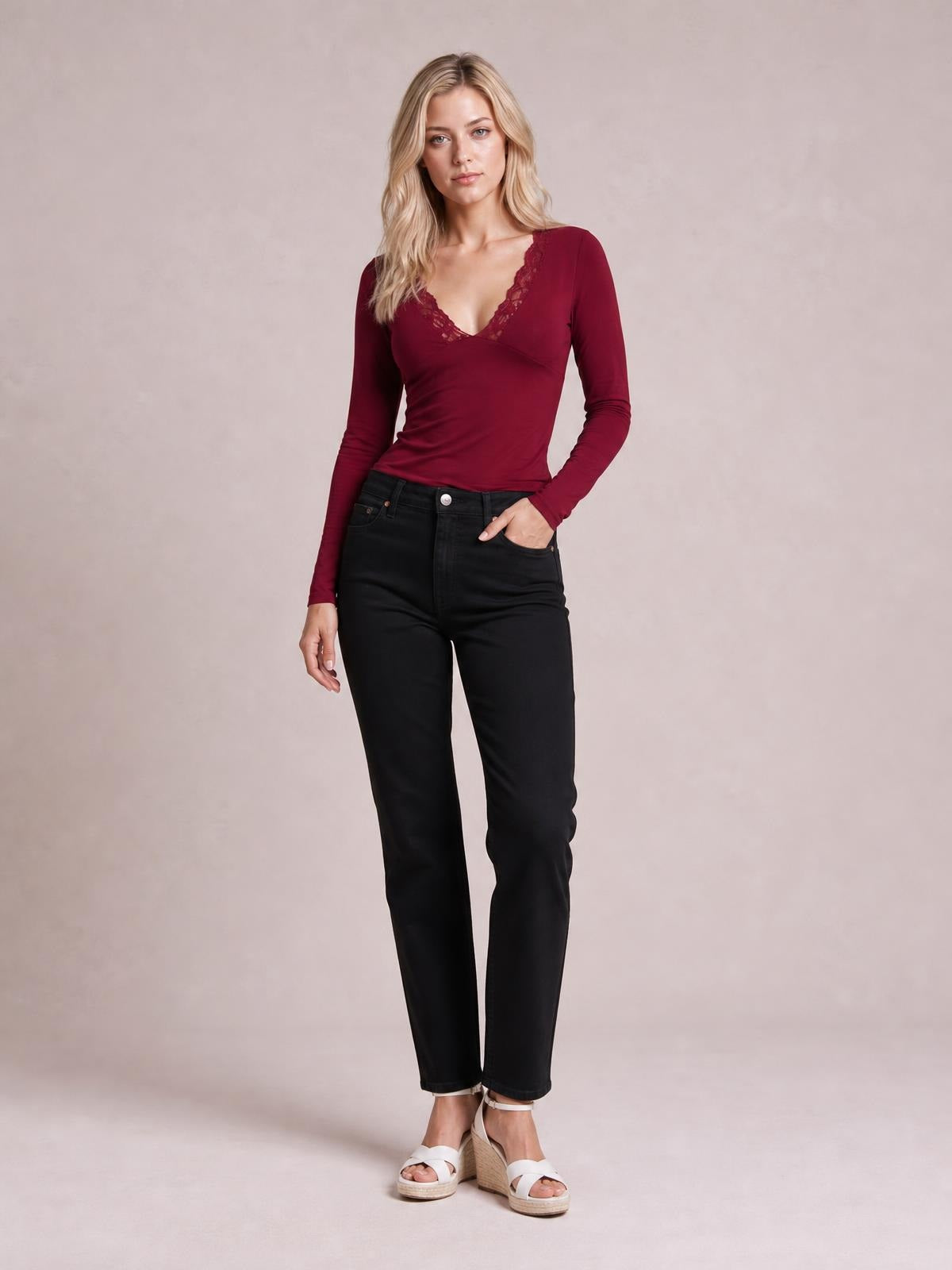 Model poses with one hand in her pocket wearing a burgundy lace detail V-neck long sleeve T-shirt with a fitted silhouette.