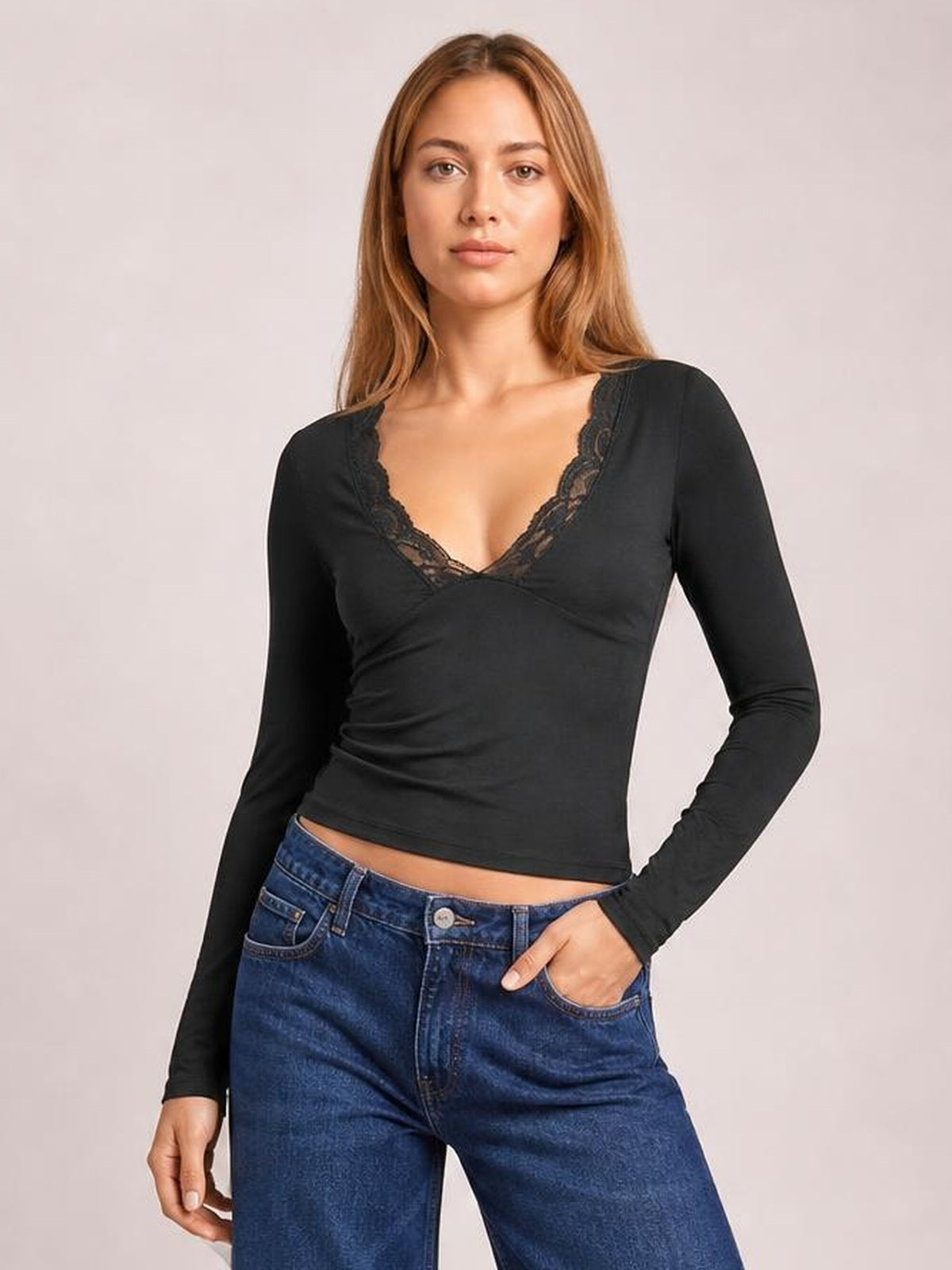 Model wearing a black lace detail V-neck long sleeve T-shirt with a fitted, slightly ruched silhouette and one hand in her jeans pocket.