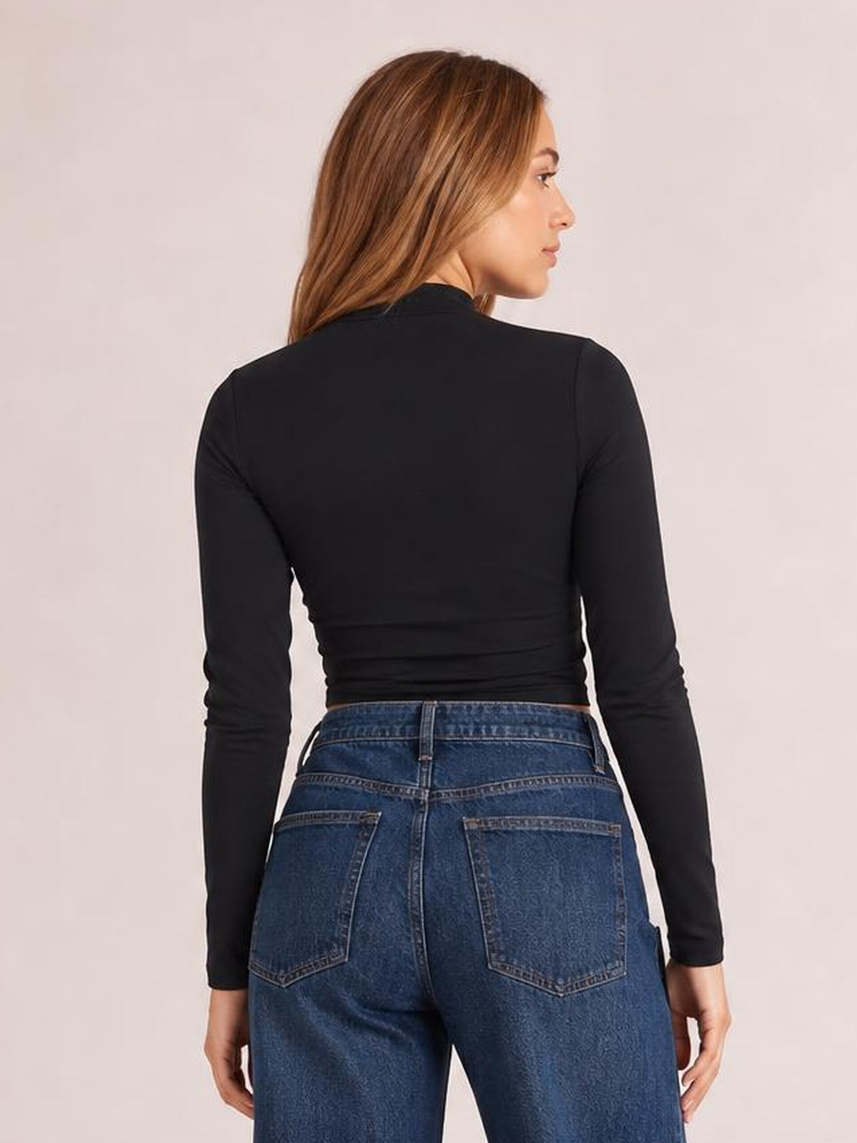 A model looks over her shoulder wearing a fitted black long-sleeve T-shirt with a smooth, close-fitting silhouette and cropped hem.