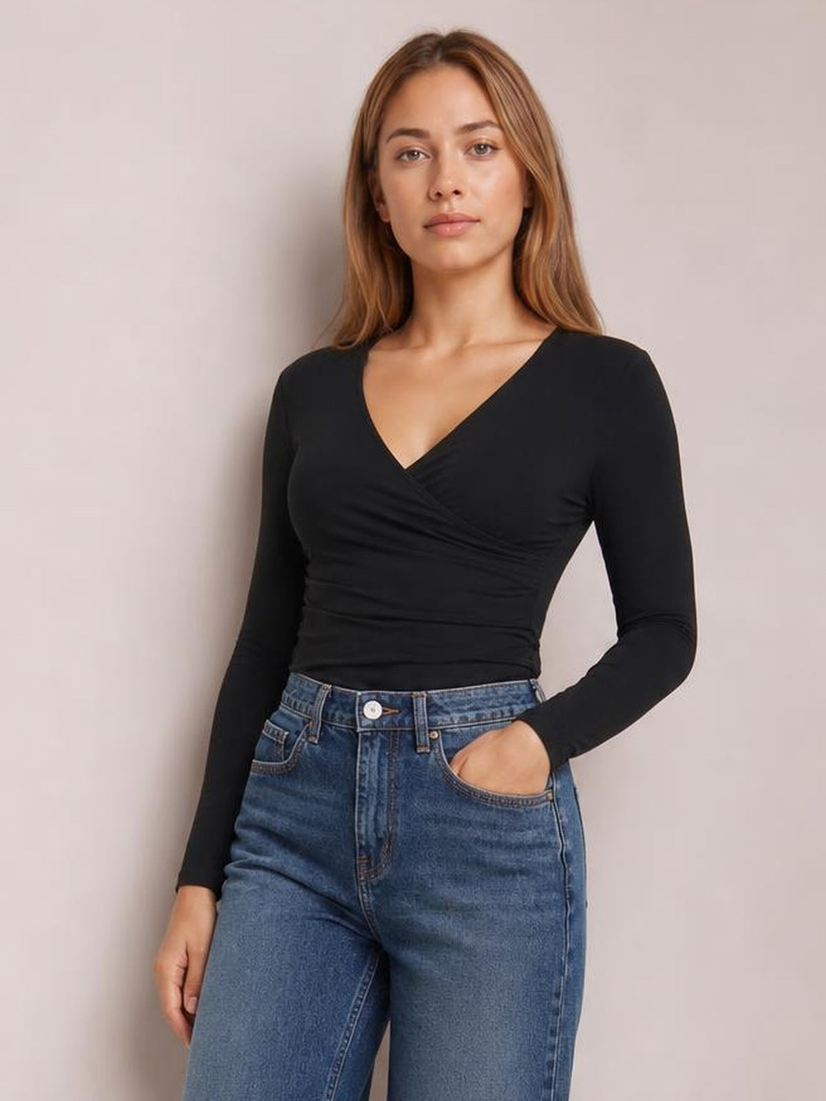 Model poses in a black long-sleeve V-neck T-shirt with a fitted silhouette, ruched wrap-style bodice, and one hand tucked into her jeans pocket.