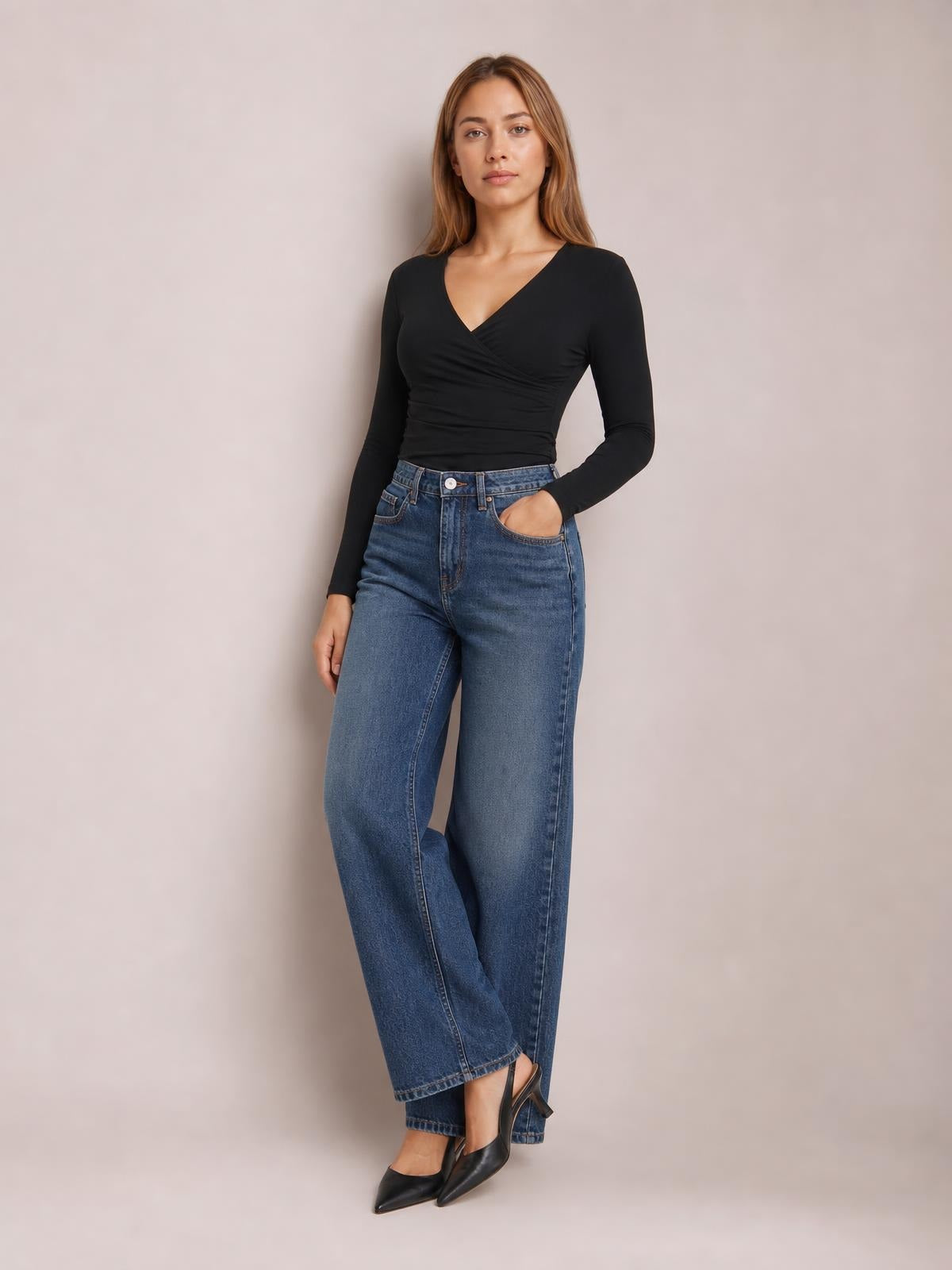 A model wears a black V-neck long-sleeve T-shirt with a fitted, gathered wrap-front silhouette, posing with one hand in her jeans pocket.