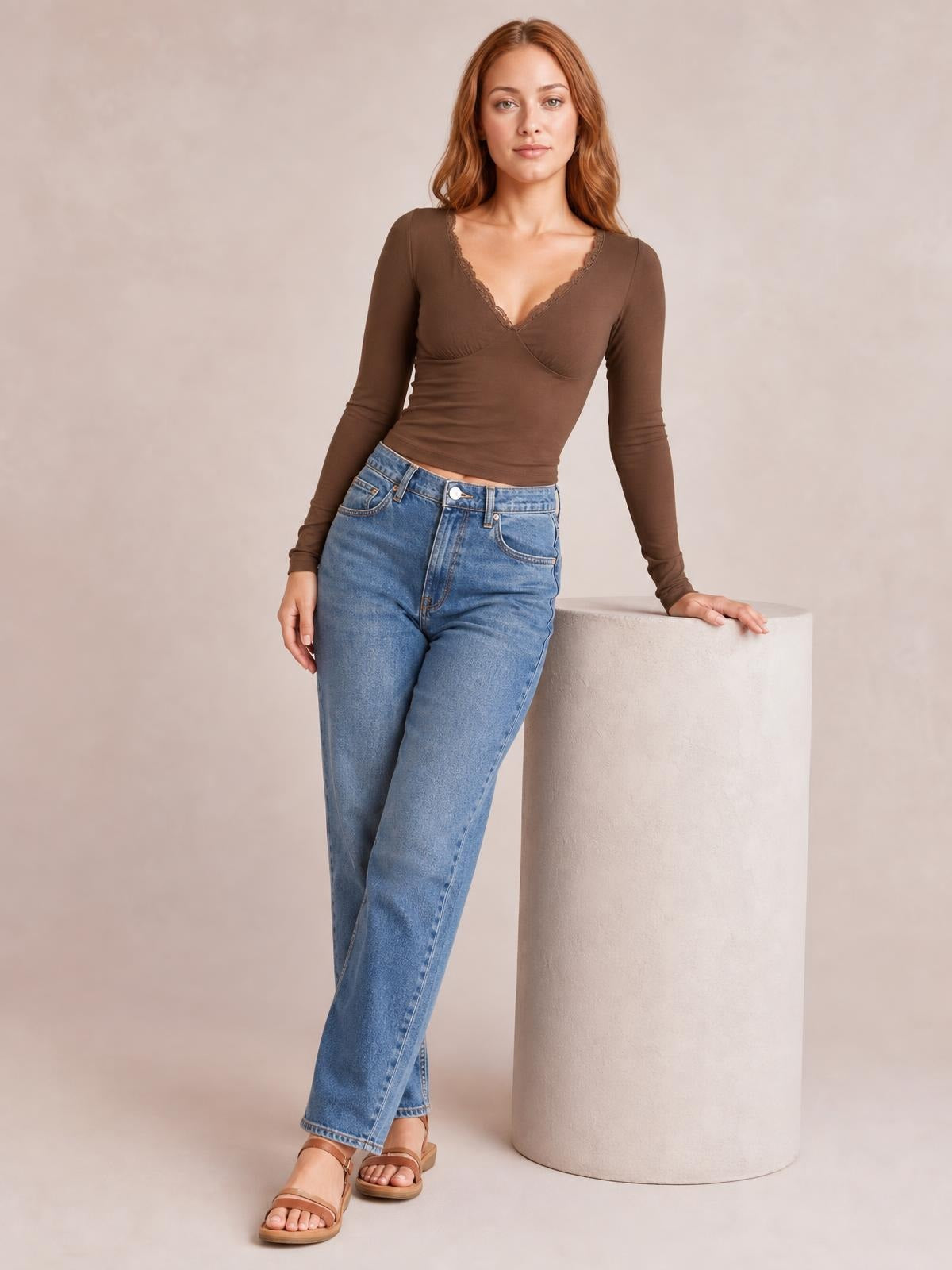A model poses in a fitted brown lace detail V-neck long sleeve T-shirt with a softly curved hem and one hand resting on a pedestal.