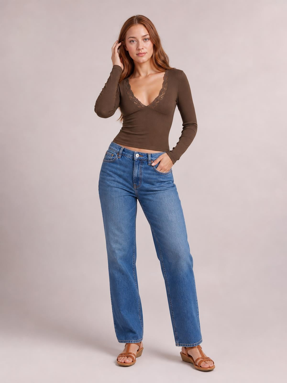 Model wears a brown lace detail V-neck long sleeve T-shirt with a fitted silhouette and ribbed construction, posing with one hand in her jeans pocket.