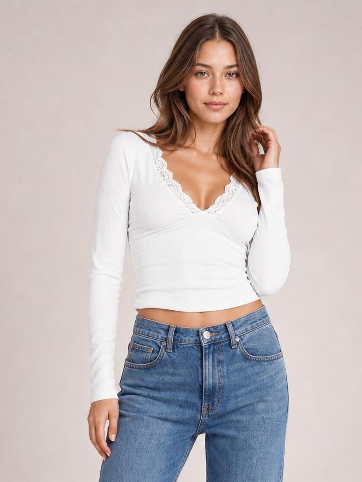 Model wearing a white lace-detail V-neck long-sleeve T-shirt with a fitted silhouette, standing with one hand touching her hair.