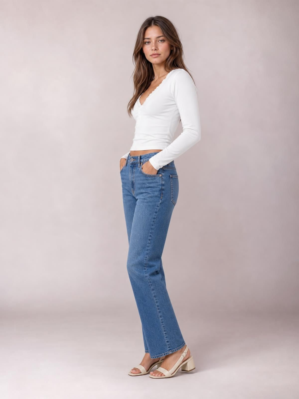 A model poses with one hand in her jeans pocket, wearing a fitted white long-sleeve T-shirt with a lace-trimmed V-neck and smooth silhouette.