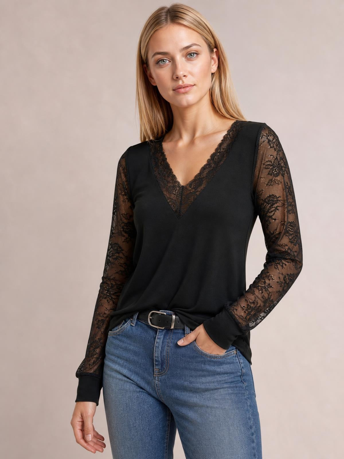 Model wearing a black lace detail V-neck long sleeve top with semi-sheer floral lace sleeves, fitted silhouette, and ribbed cuffs, posing with one hand in her jeans pocket.