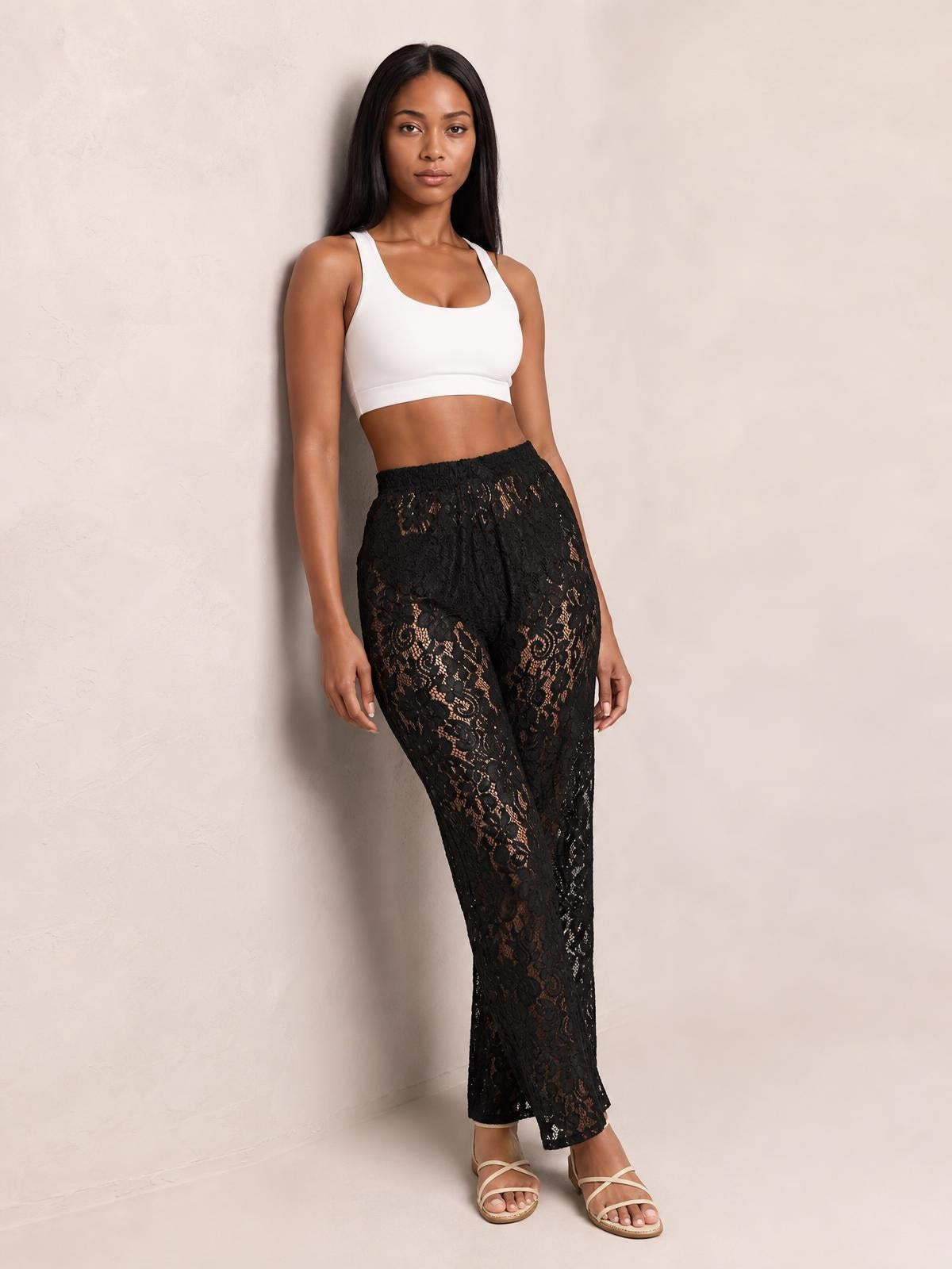 Model poses in black high-waist lace swim pants with a relaxed straight-leg silhouette, elastic waistband, and semi-sheer patterned construction.