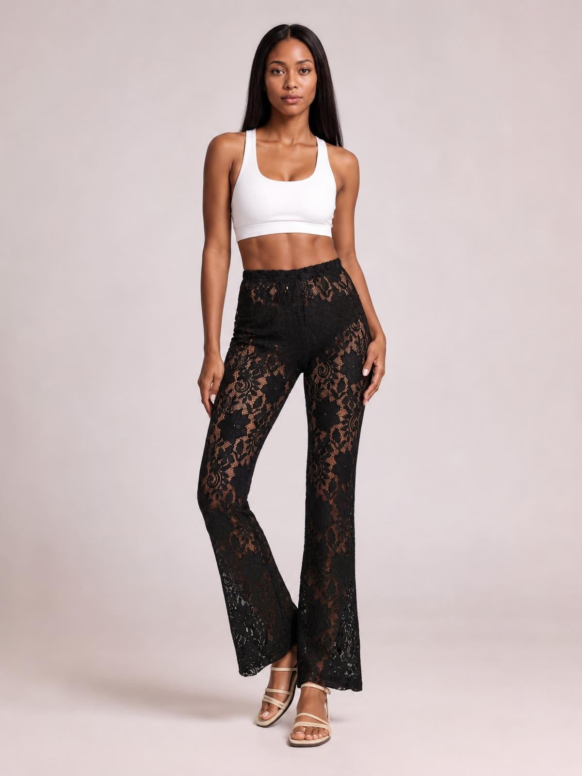 Model stands with one leg crossed in black lace high-waist swim pants featuring a gathered waistband and wide-leg silhouette, paired with a white cropped tank top.