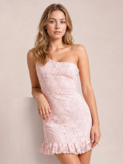 Model poses in a pale pink lace one-shoulder mini dress with a fitted silhouette, floral construction, and ruffled hem.