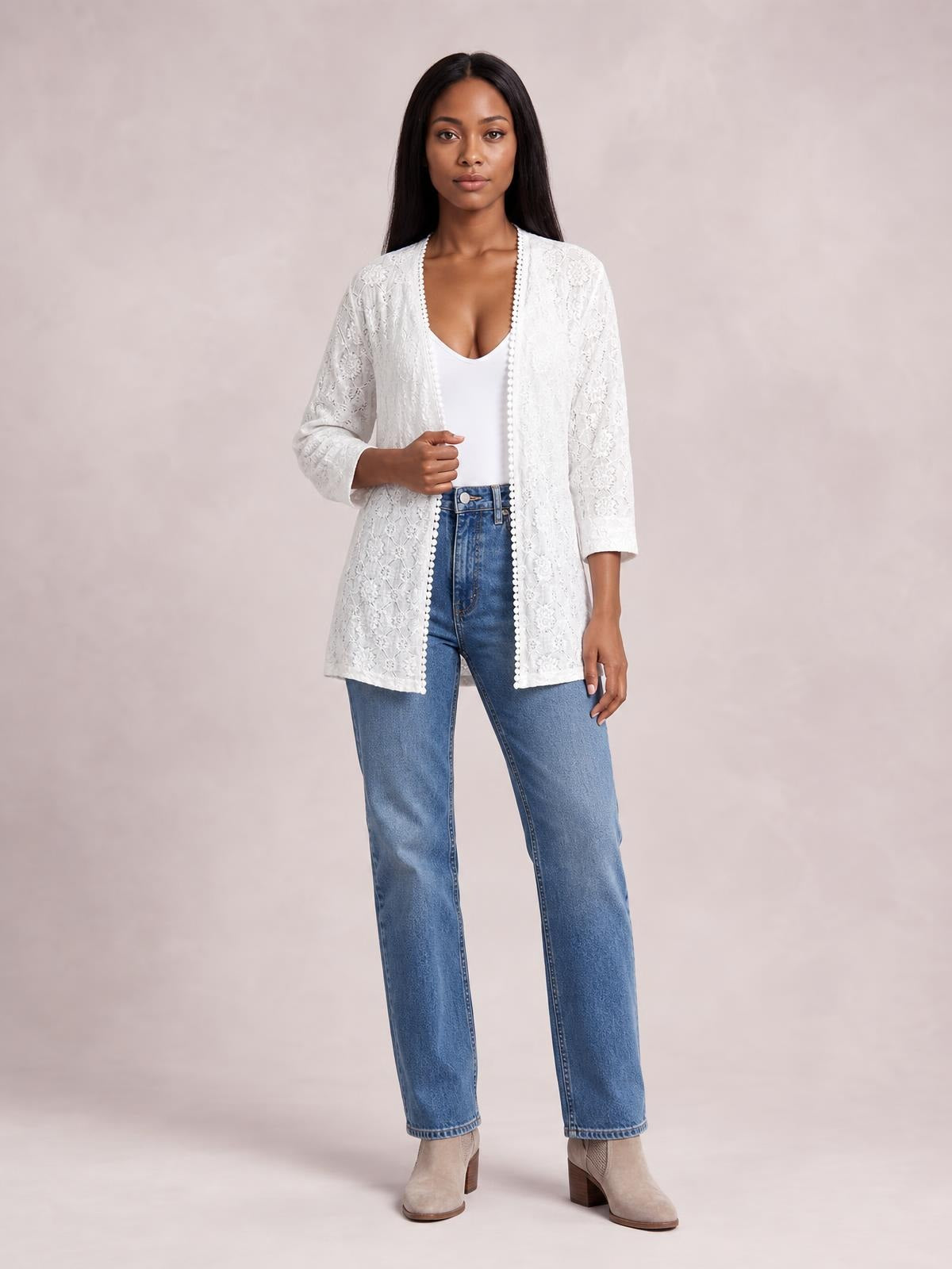 Model poses in a white lace open front cover up with three-quarter sleeves, scalloped trim, and a long relaxed silhouette over a white top and jeans.