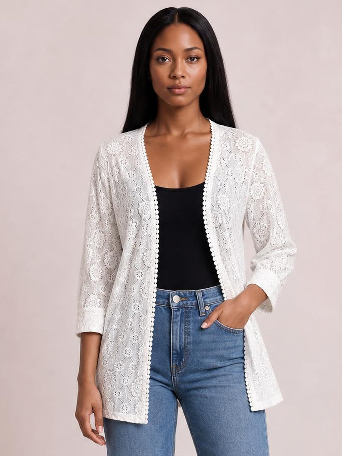 Model wearing a white lace open front cover up with a longline silhouette, three-quarter sleeves, and scalloped trim over a black top and jeans.