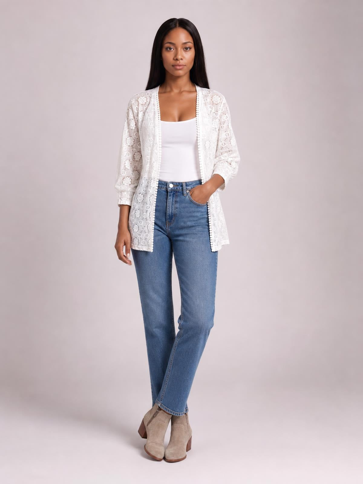 Model in a relaxed pose wears a white lace open-front cover up with long sleeves, floral texture, scalloped trim, and a straight, mid-thigh silhouette.