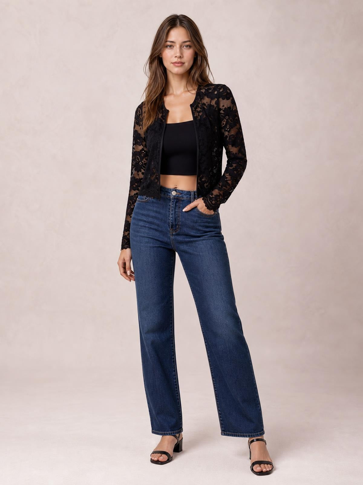 Model wearing a black lace open-front long-sleeve jacket with sheer floral construction and a fitted silhouette, posed with one hand in her jeans pocket.